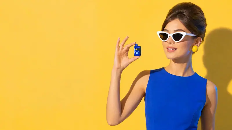 Adult woman holding a WINDBAR SPECTRUM in Cobalt Blue between her fingers, yellow wall (WindBar.ai)
