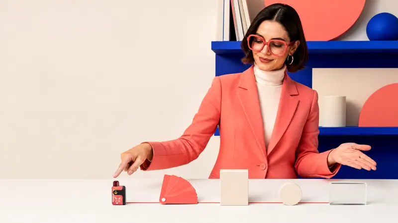 Adult woman in coral blazer presenting a WINDBAR SPECTRUM in Coral Pop on a desk (WindBar.ai)